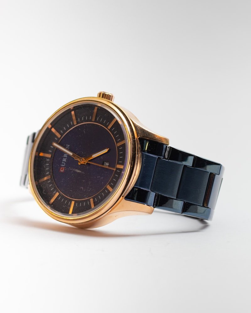 Rose gold cased wristwatch with a navy blue link bracelet on a white background